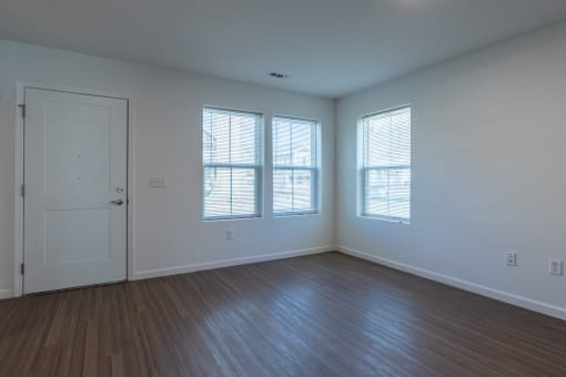 an empty living room with a door and three windows