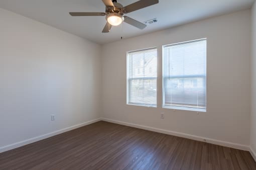 an empty bedroom with a ceiling fan and two windows