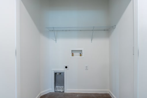 a hallway with white walls and a white door and a shelf on the ceiling