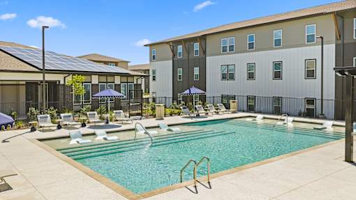 Pool at The Esther apartments in Converse, TX with tanning deck, lounge seating and umbrellas.