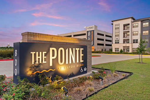 The Pointe at Bayouapartment community entrance featuring branded monument signage, landscaped grounds, contemporary residential architecture, and a welcoming arrival experience.