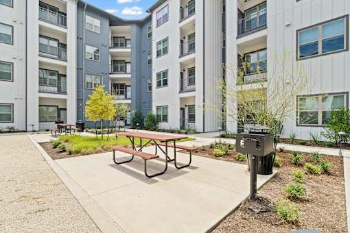 Apartment community courtyard featuring outdoor gathering spaces, landscaped grounds, pedestrian pathways, and contemporary multifamily residential architecture.