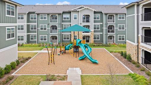 A playground area with a slide in front of apartment buildings.