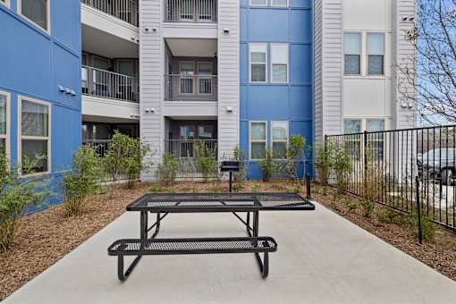 A black picnic table is in the foreground of a courtyard with a blue building in the background.