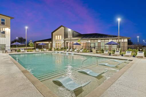 Sunset view of pool at The Esther apartments in Converse, TX with tanning deck, lounge seating and umbrellas.