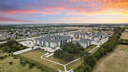 Sunset aerial view of Aviator 1518 apartments in Schertz, TX surrounded by trees and landscaped green space.