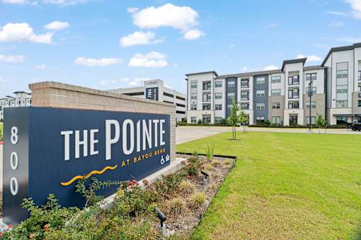 Apartment community entrance featuring branded monument signage, landscaped grounds, contemporary residential architecture, and a welcoming arrival experience.