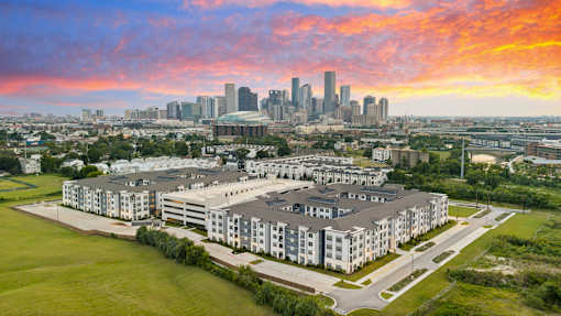 Apartment community exterior highlighting architectural design, structured parking, landscaped open areas, and a dynamic city backdrop.