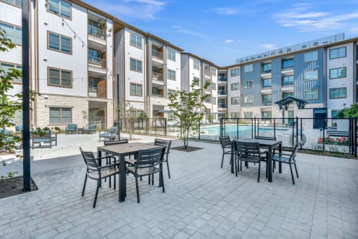 a patio with tables and chairs in front of an apartment building