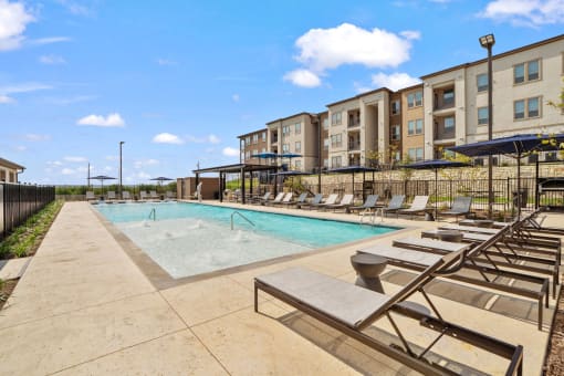a pool with lounge chairs and an apartment building