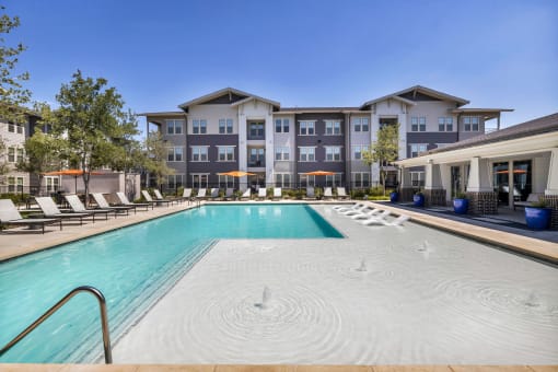 a swimming pool with lounge chairs and umbrellas in front of an apartment building