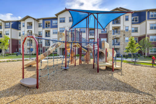 a playground with a swing set and slides in front of an apartment building