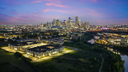 Multifamily residential community featuring contemporary apartment buildings, illuminated streetscapes, landscaped grounds, and a thoughtfully planned site layout at dusk.