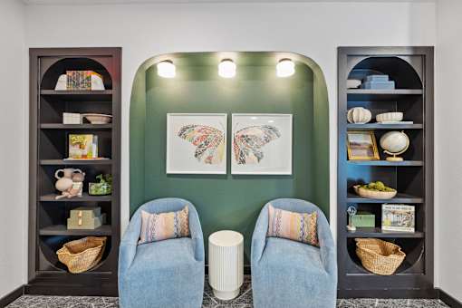 Two blue chairs are placed in front of a green wall with a picture and shelves.