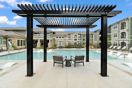 A pool area with a black pergola and lounge chairs.