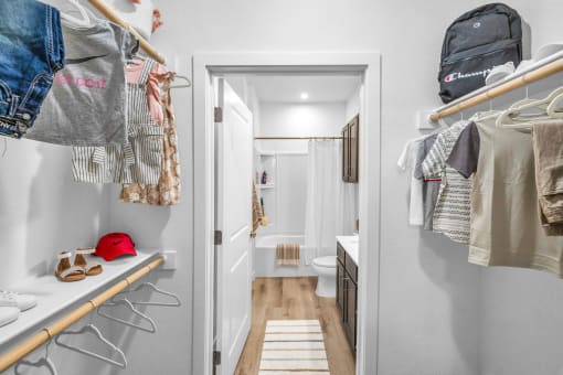 a walk -in closet with a bathroom in the background