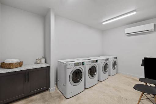 A laundry room with three washing machines and a cabinet.
