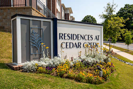 Community monument sign displaying “Residences of Cedar Creek,” set on a stone base with surrounding landscaping and greenery near the property entrance.