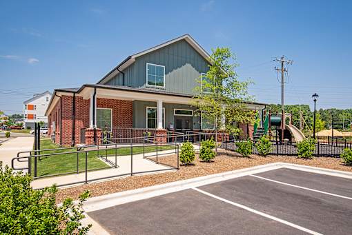 Community building exterior with a mix of brick and siding, showcasing a covered entry, walkway with ramp access, and adjacent playground equipment.