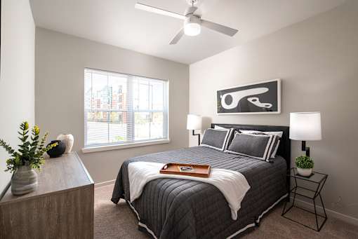Bright bedroom interior with a central bed, decorative pillows, and a wall art piece above, accented by a window allowing natural daylight into the space.