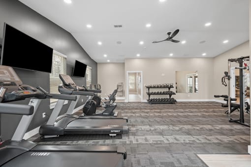 a gym with treadmills and televisions on the wall