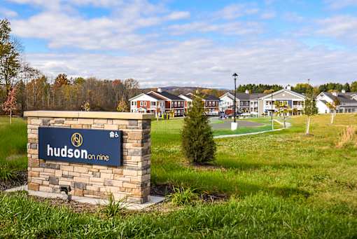 A sign for Hudson on Nine stands in front of a grassy field.