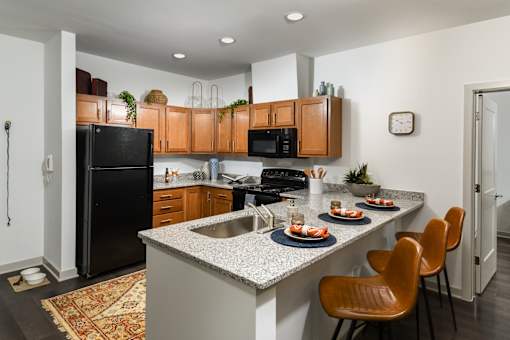 A kitchen with a black refrigerator, brown cabinets, and a white countertop.