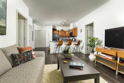 Open-concept apartment living room and kitchen with wood floors, breakfast bar seating, and modern finishes.