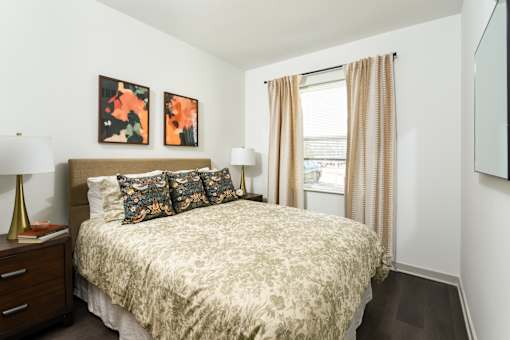 Bright, modern bedroom with a large window, soft neutral curtains, and a stylish upholstered bed paired with a cozy workspace area.
