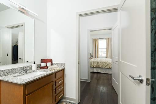 Bright bathroom vanity with granite-style countertops and wood cabinetry, connected to a bedroom through an open, easy-flow layout.