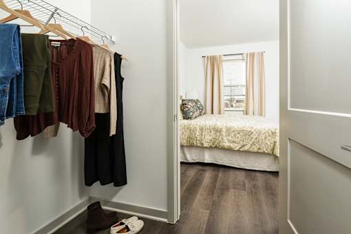 Walk-in closet with open hanging storage and easy access to a bright bedroom featuring wood flooring and natural light.