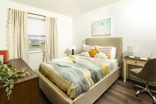 Bright, modern bedroom with a large window, soft neutral curtains, and a stylish upholstered bed paired with a cozy workspace area.