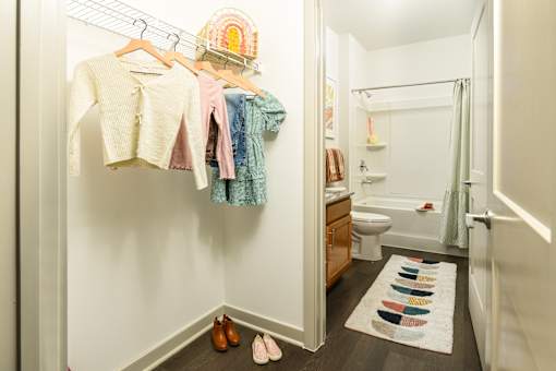 Spacious walk-in closet with open shelving and hanging storage, leading into a bright bathroom with a full tub and vanity.