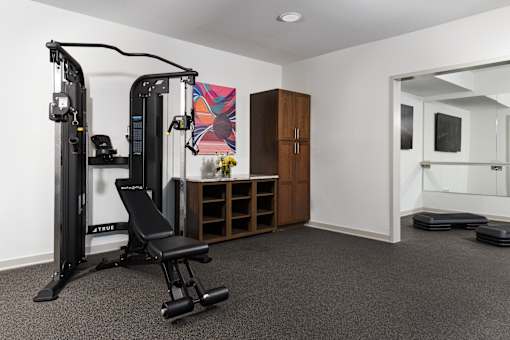 Modern fitness room with strength training equipment, open floor space, and a dedicated area for stretching or group workouts.