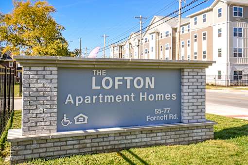 Apartment community with displayed property sign, contemporary multi-story building, surrounding fencing, and landscaped grounds.