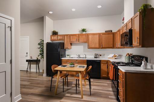 Kitchen and dining area at The Davis II in Cleveland, featuring wood cabinetry, black appliances, a breakfast bar, and a dining table with chairs.