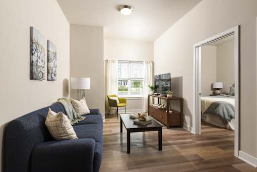 Model apartment living room at The Davis II in Cleveland, featuring a sofa, coffee table, accent chair, wood-style flooring, and large windows providing natural light.