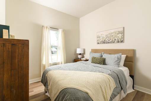 Model apartment bedroom at The Davis II in Cleveland, featuring a furnished bed with neutral bedding, bedside tables, wood-style flooring, and a window providing natural light.