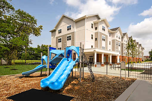 Outdoor playground at The Davis II in Cleveland, featuring bright blue slides, climbing equipment, and a mulch-covered play area beside the apartment building.