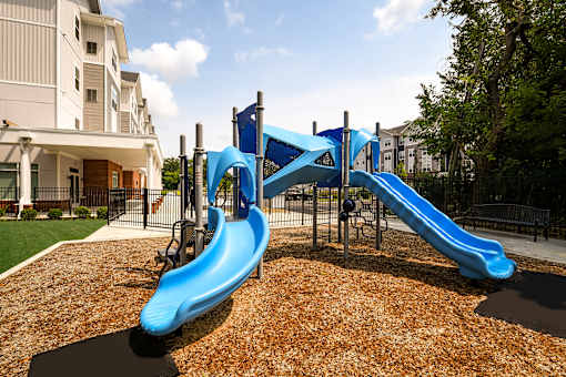 Outdoor playground at The Davis II in Cleveland, featuring blue slides and climbing equipment over a mulch-covered play area.