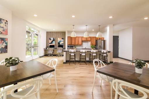 Community room at The Davis II in Cleveland, featuring tables and chairs, lounge seating, a kitchen area with wood cabinetry, and large windows providing natural light.