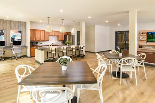 A community room with a  kitchen and dining tables and chairs.