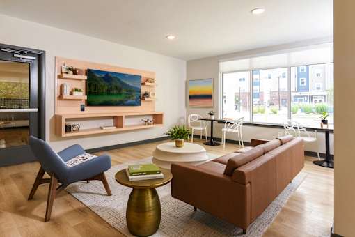 A community room with a brown couch, a blue chair, and a painting on the wall.