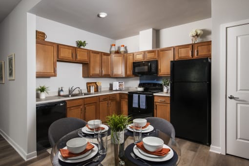 a kitchen with black appliances and wooden cabinets and a table with plates and chairs