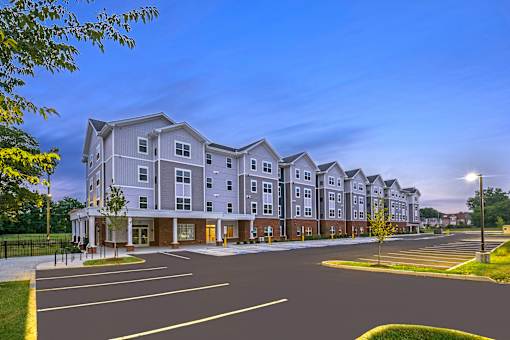 Exterior view of The Davis II in Cleveland, featuring a multi-story apartment building with light-colored siding, brick accents, covered entrances, and a paved parking area in front.