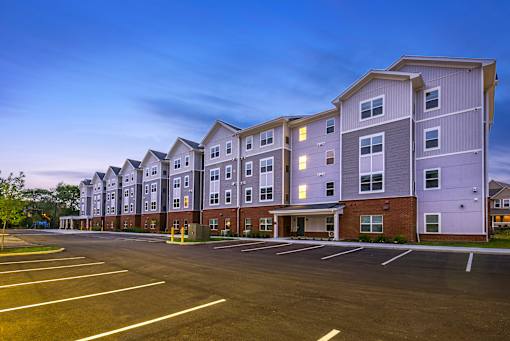 Exterior view of The Davis II in Cleveland, featuring a multi-story apartment building with brick accents and light-colored siding, with a paved parking lot in the foreground.