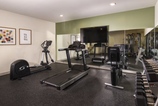 a gym with cardio equipment and a flat screen tv