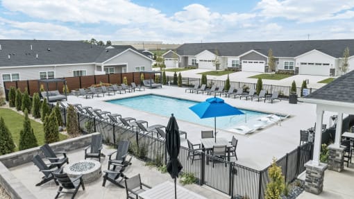 a swimming pool with patio furniture and umbrellas in front of houses