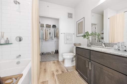 A bathroom with a white tub, wooden floor, and a white toilet.