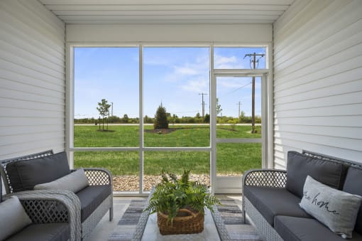 a screened porch with two couches and a plant in front of a large window